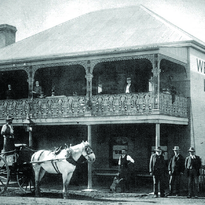 A black and white photo of a horse drawn carriage in front of a building.